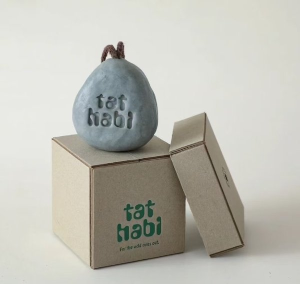 Unique gray pear-shaped item with "tat habi" logo on minimalist kraft packaging