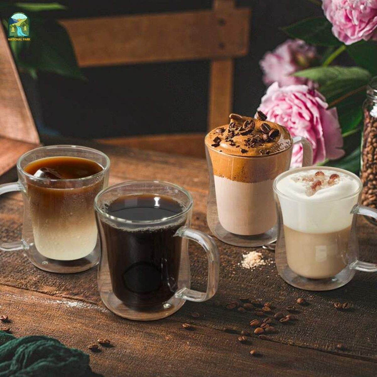 Four glass mugs with various coffee drinks on a wooden table with flowers and coffee beans