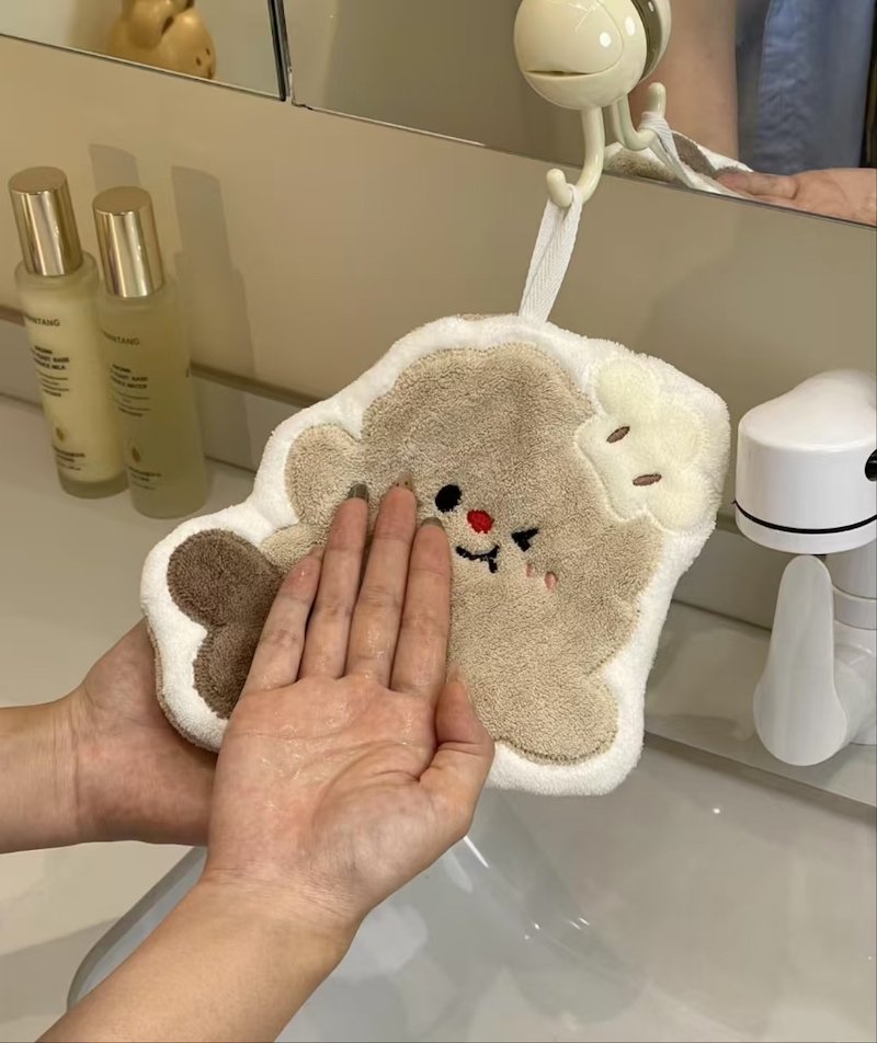 Cute bear-shaped hand towel hanging in a bathroom with a person washing hands