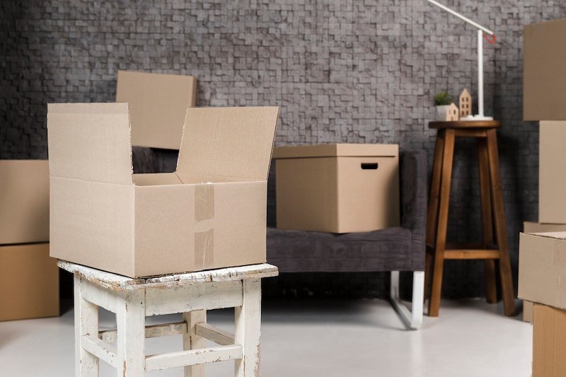 Open cardboard box on a stool in a modern room with various packed boxes