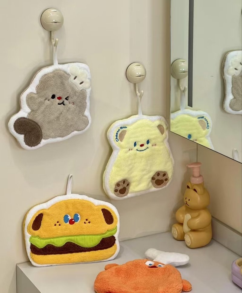 Cute character-shaped hand towels hanging in a bathroom, including bear and burger designs