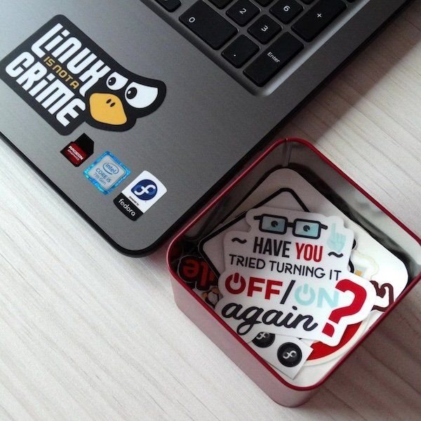 Laptop with Linux-themed sticker and a tin box of tech-related stickers