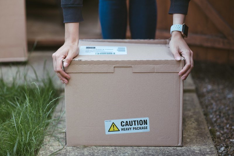Person lifting a cardboard box with a caution heavy package label
