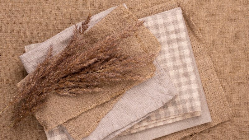 Stack of natural linen fabrics with dried grass on a burlap background