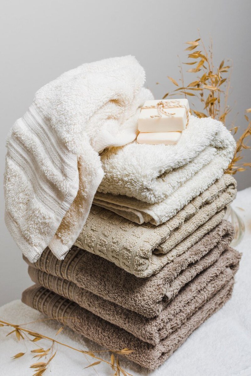 Stack of neutral-toned towels with handmade soap and dried plant decor