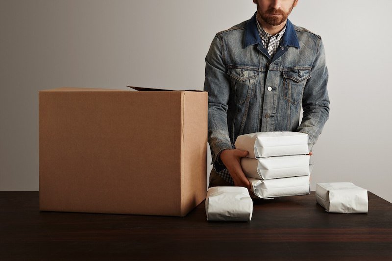 Man in denim jacket packing wrapped items into a cardboard box