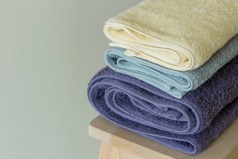 Stack of rolled towels in yellow, blue, and purple on a wooden stool