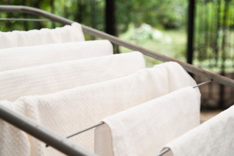 White towels hanging on a drying rack outdoors with a garden background