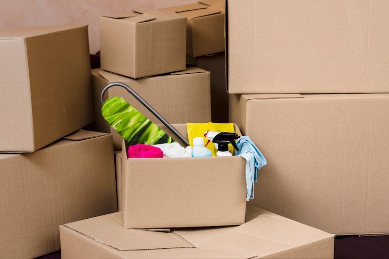 Cardboard boxes stacked with one open box containing cleaning supplies