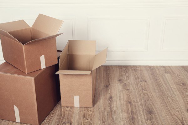 Open and closed brown cardboard boxes on a wooden floor against a white wall