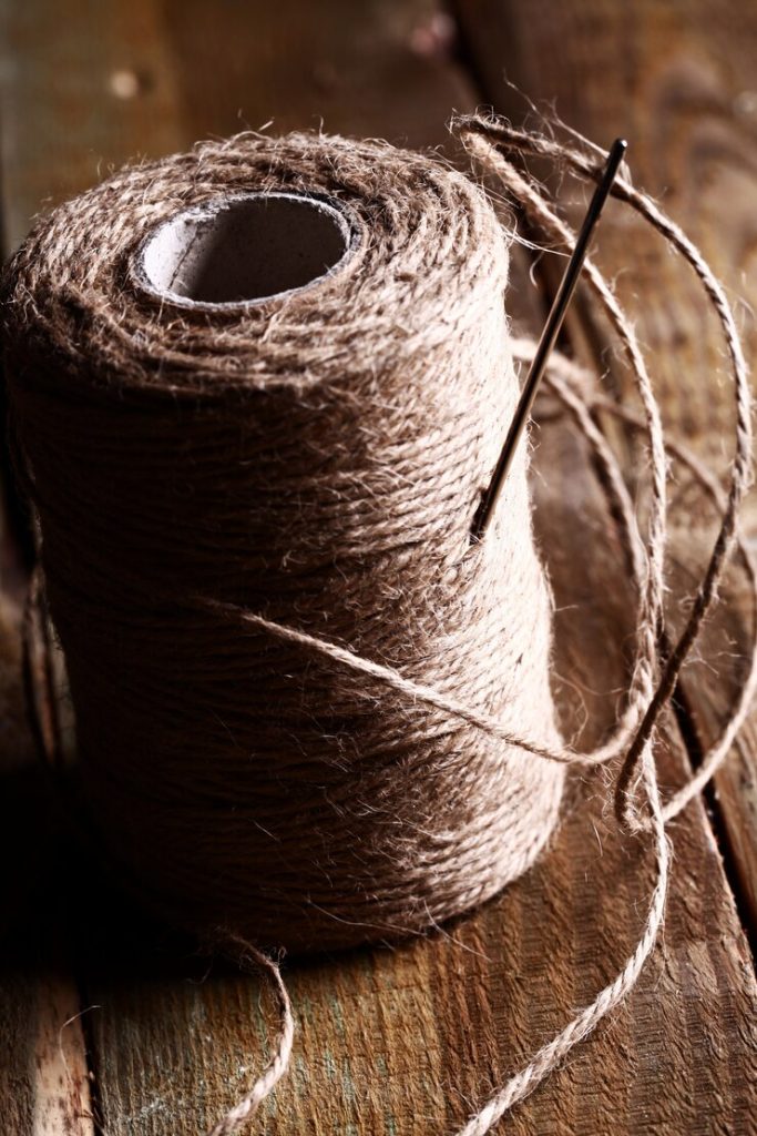 Sewing needles and natural thread arranged on a wooden table