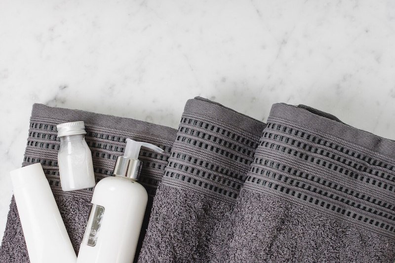 Gray textured towels with white bottles and toiletries on a marble surface