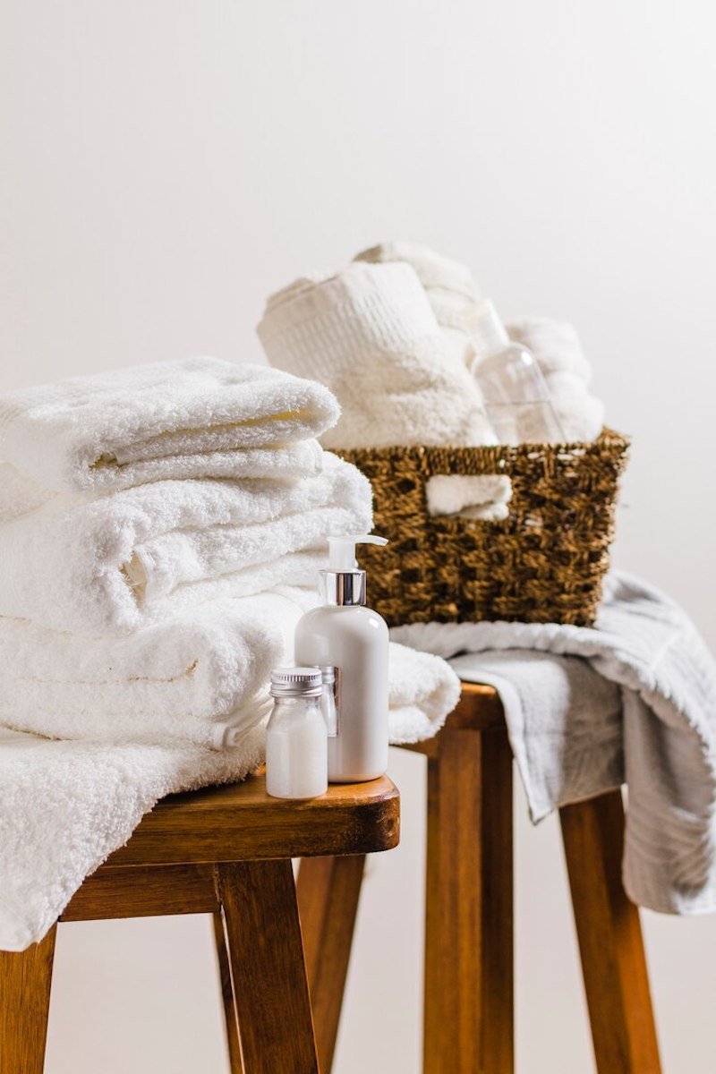 Stacked white towels with toiletries on wooden tables, next to a wicker basket
