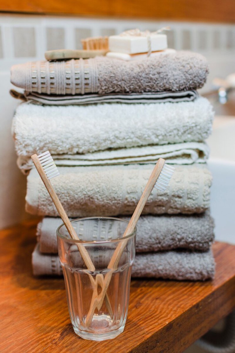 Stacked beige towels with wooden toothbrushes in a glass, placed on a wooden countertop