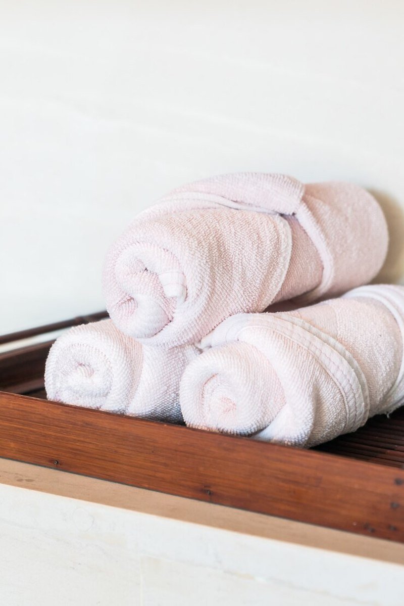 Three rolled pink towels neatly stacked on a wooden tray