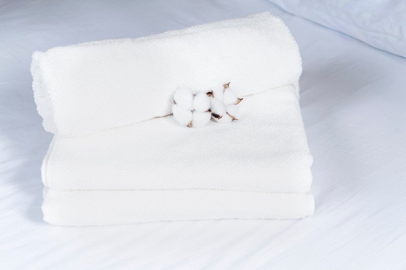 Folded white towels with a cotton flower placed on a bed