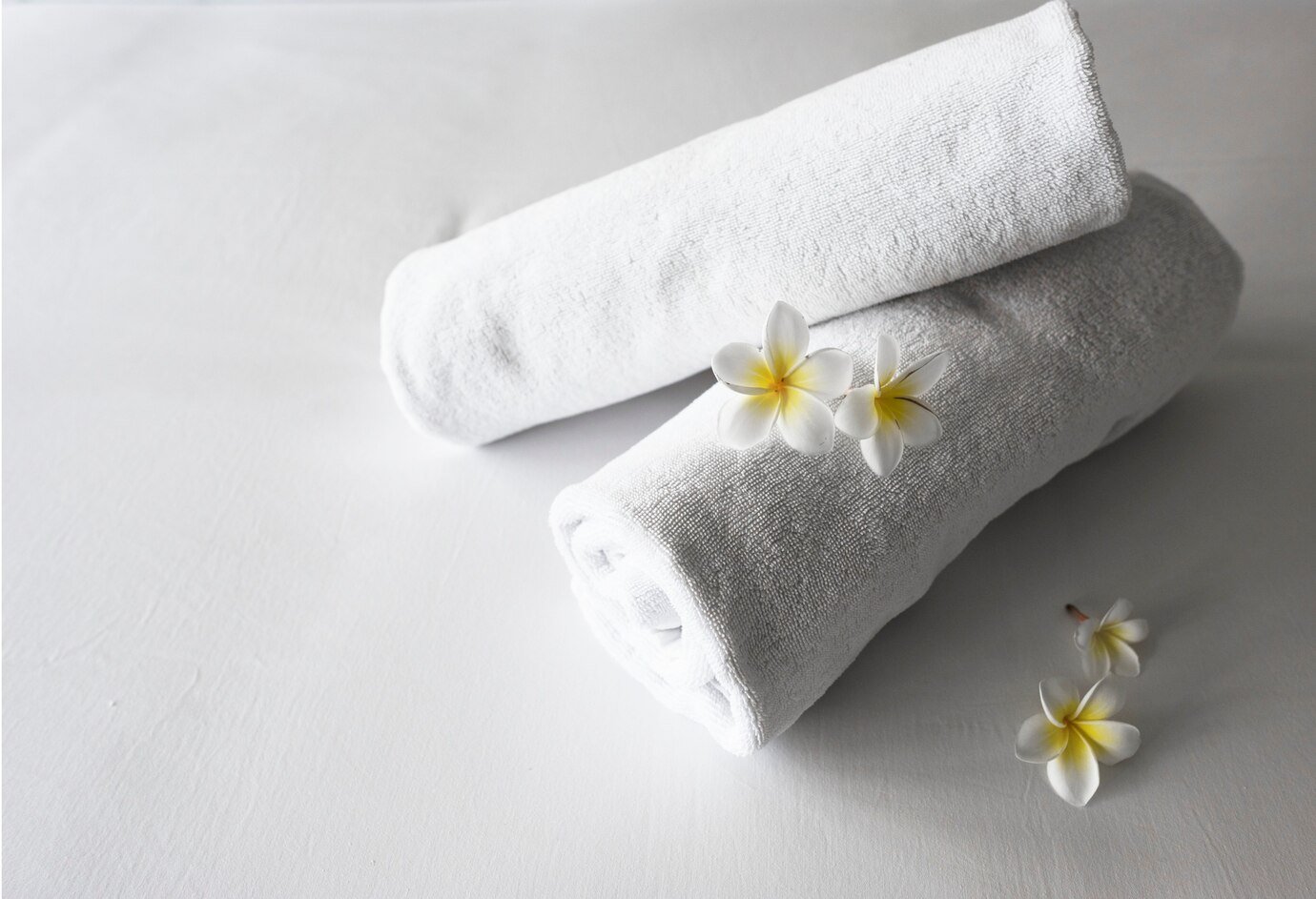 Rolled white towels with fresh frangipani flowers on a white surface