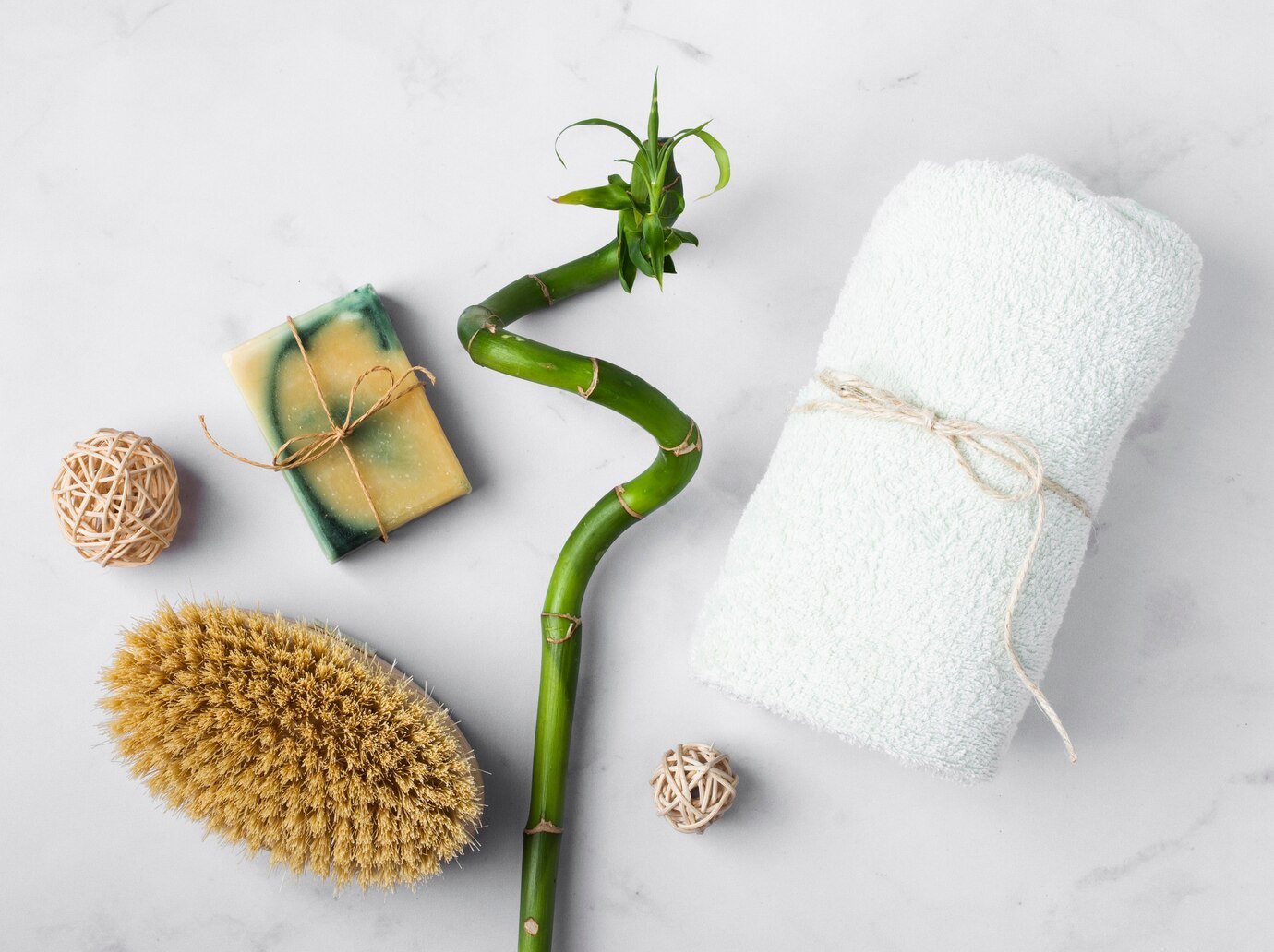 Eco-friendly spa items: green bamboo, natural soap, brush, and rolled towel on marble