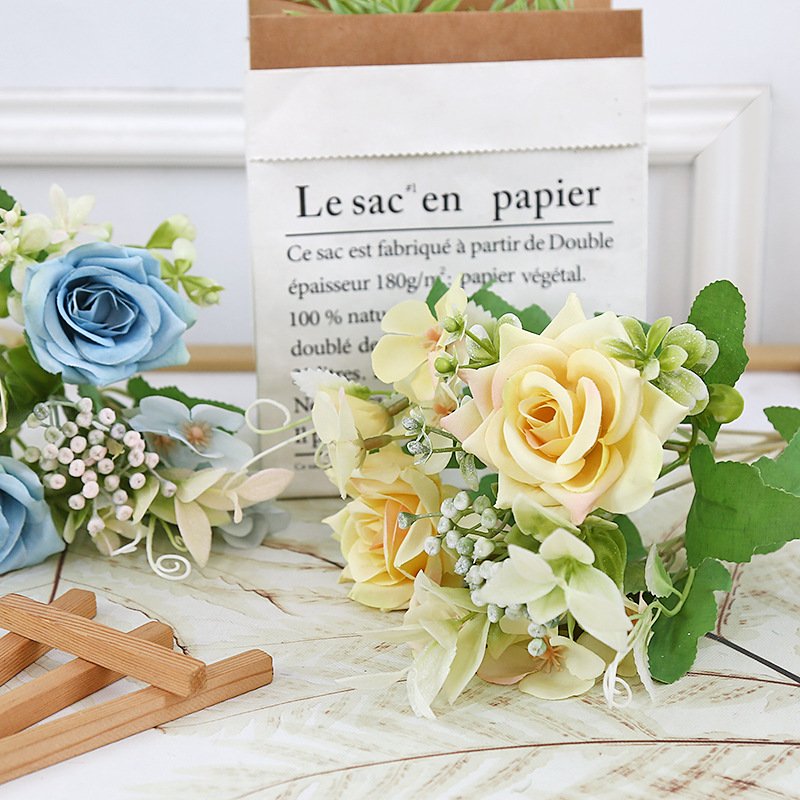Blue and yellow paper flowers arranged beside a paper bag and sticks