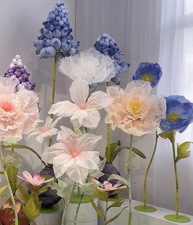 Delicate paper flowers with soft pastel colors and green stems in a decorative arrangement